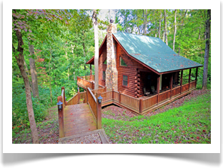 side view of cabin with tall green leave trees and stairs to wrap around porch
