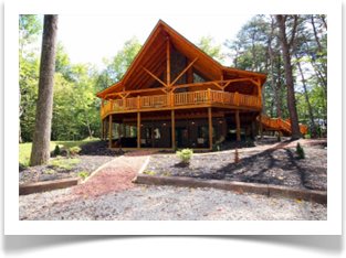 tall trees surronding two story lodge with 4 windows, wrap around deck